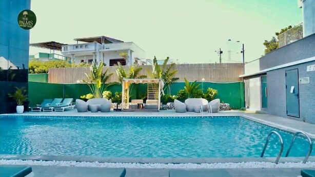 A swimming pool with lounge chairs, a pergola, and a building in the background.