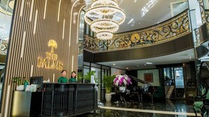 A hotel lobby with a reception desk, a grand chandelier, and a staircase leading to an upper level.