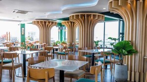 A modern restaurant interior with high wooden columns, green upholstered chairs, and large windows offering a view.