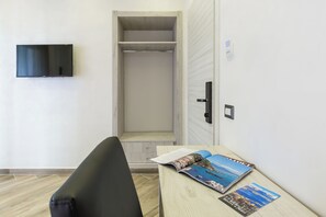 Una habitación con cama, televisión montada en la pared, una mesa de madera con revistas y un armario con puerta.