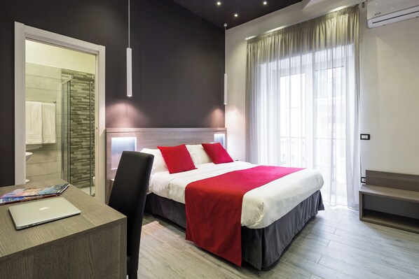 A modern hotel room with a large bed, a desk with a laptop, and a view of the city through large windows. - Hotel Bella Napoli (Naples)