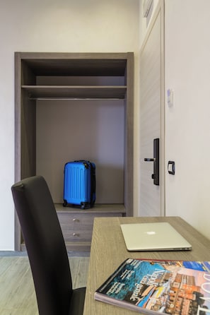A hotel room with a wooden wardrobe, a blue suitcase, a laptop, and a magazine on the table. - Hotel Bella Napoli (Naples)