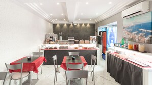 A breakfast area with a buffet, tables, chairs, and a large window with a cityscape view. - Hotel Bella Napoli (Naples)
