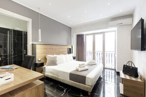 A modern hotel room with a large bed, a wooden desk, a TV, and a balcony with a view. - Hotel Bella Napoli (Naples)