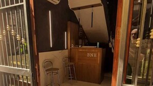 A hotel interior with a reception desk labeled "BNH," two bar stools, and a staircase leading to an upper floor. - Hotel Bella Napoli (Naples)