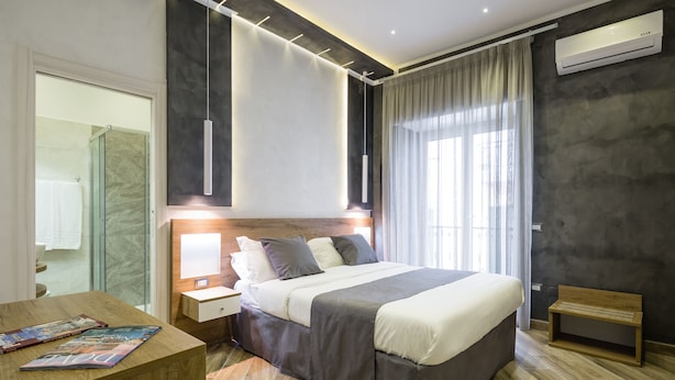 A modern hotel room with a large bed, bedside tables, a wooden bench, and a magazine on the side table. - Hotel Bella Napoli (Naples)