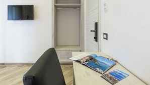 A room with a bed, a TV mounted on the wall, a wooden table with magazines, and a closet with a door. - Hotel Bella Napoli (Naples)