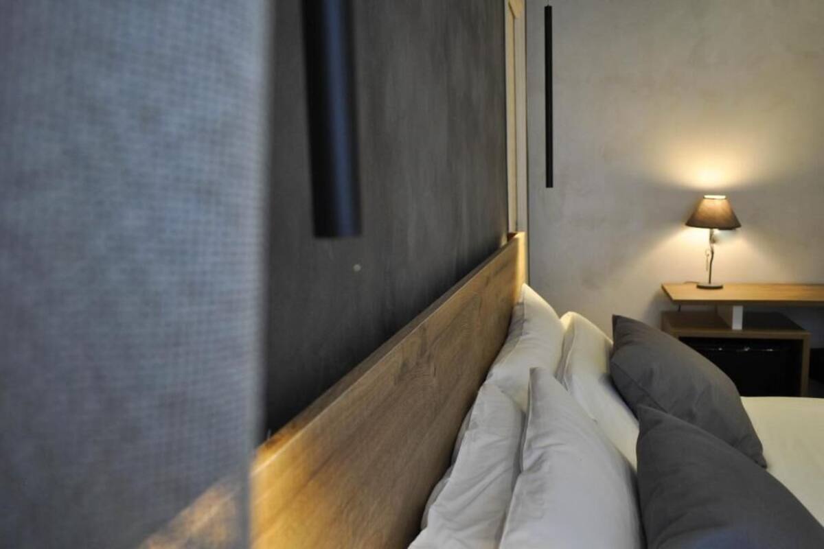 A bedroom with a wooden headboard, a bedside table with a lamp, and a wall-mounted light fixture.