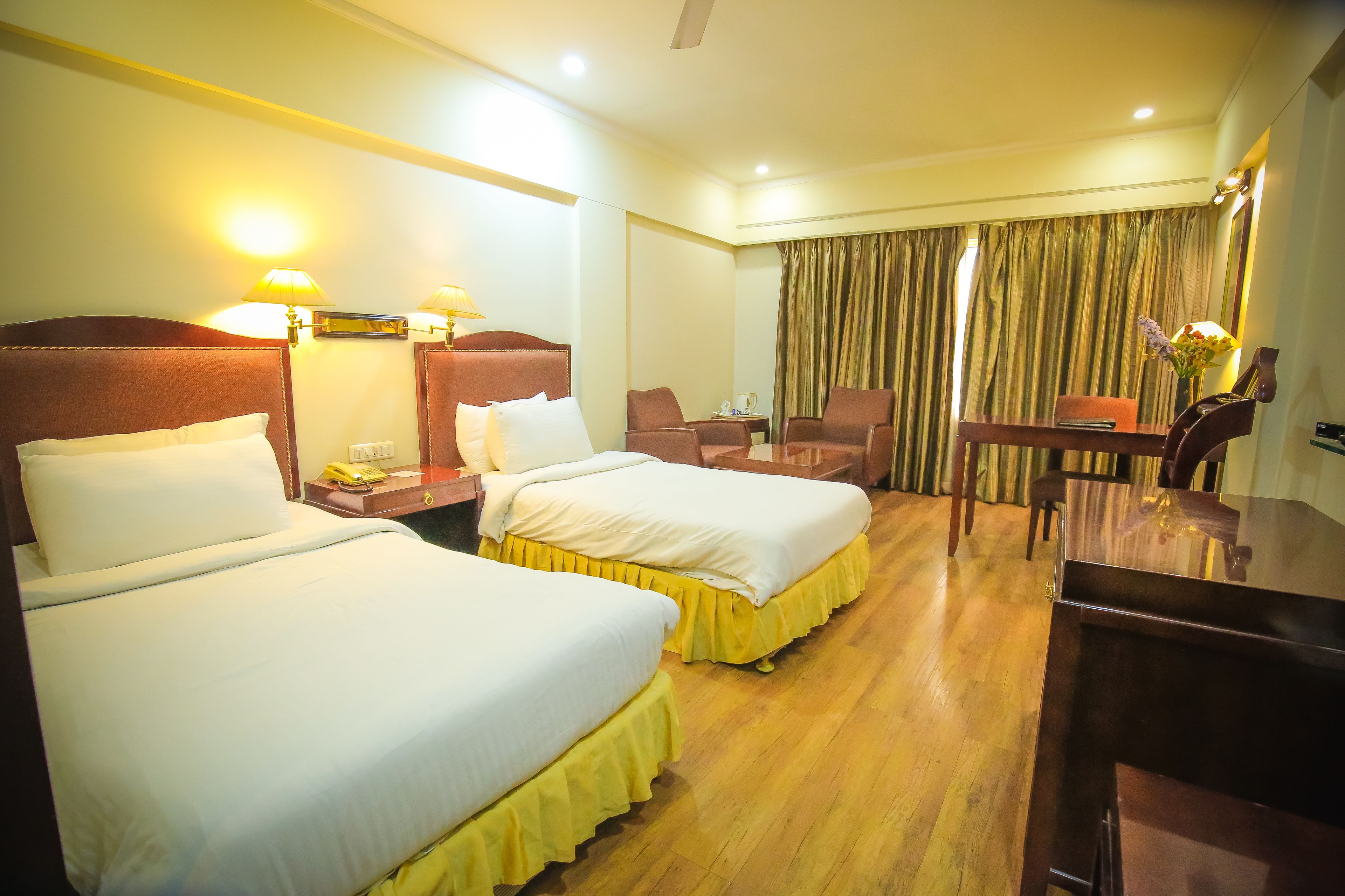 A hotel room with two beds, a desk, a chair, and a table.
