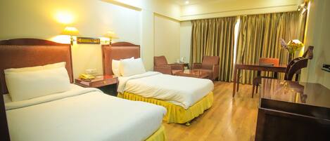 A hotel room with two beds, a desk, a chair, and a table.