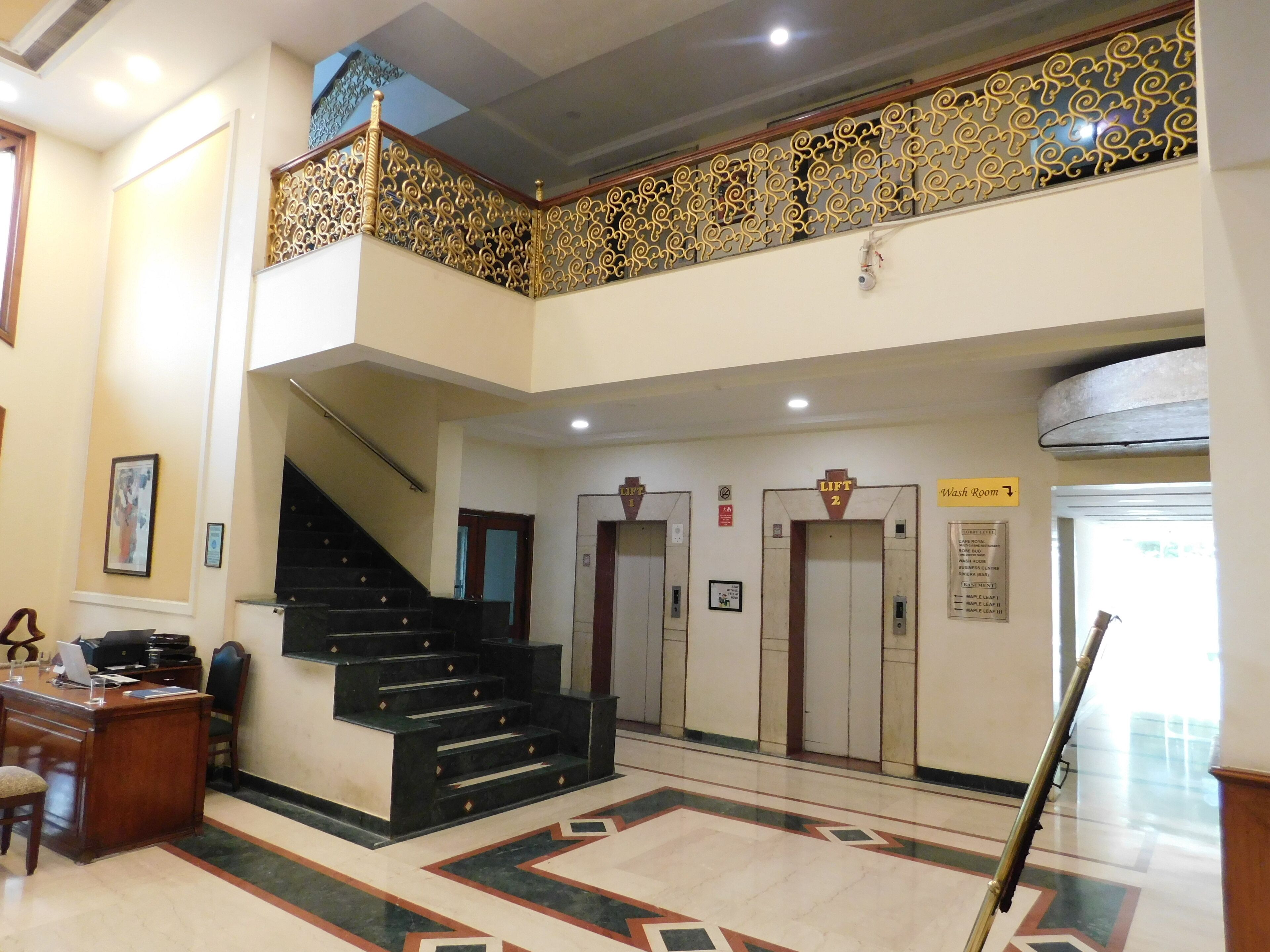 A hotel lobby with a staircase, elevators, and a reception desk.