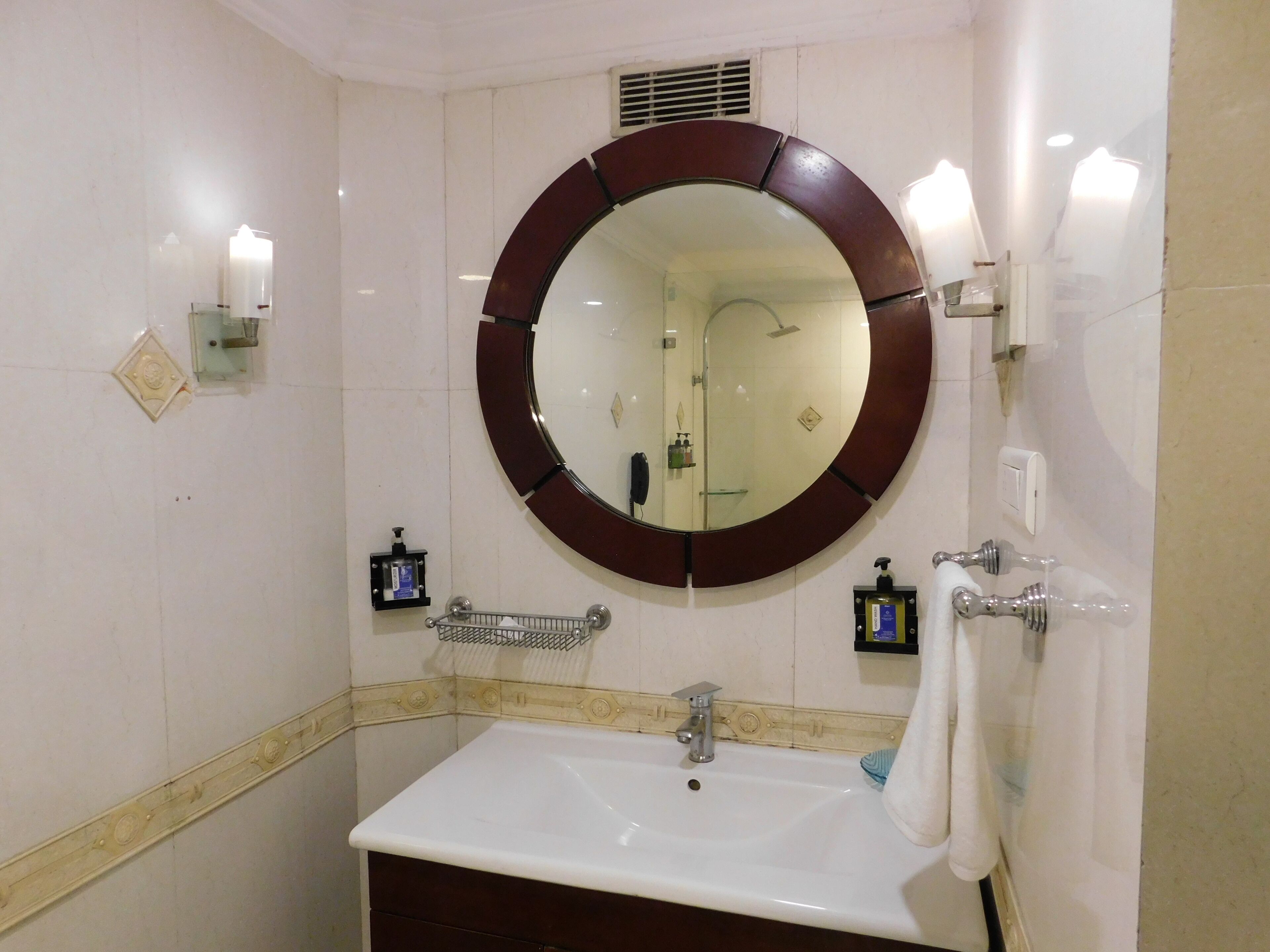 Un baño con un espejo redondo, un lavamanos y un perchero para toallas.