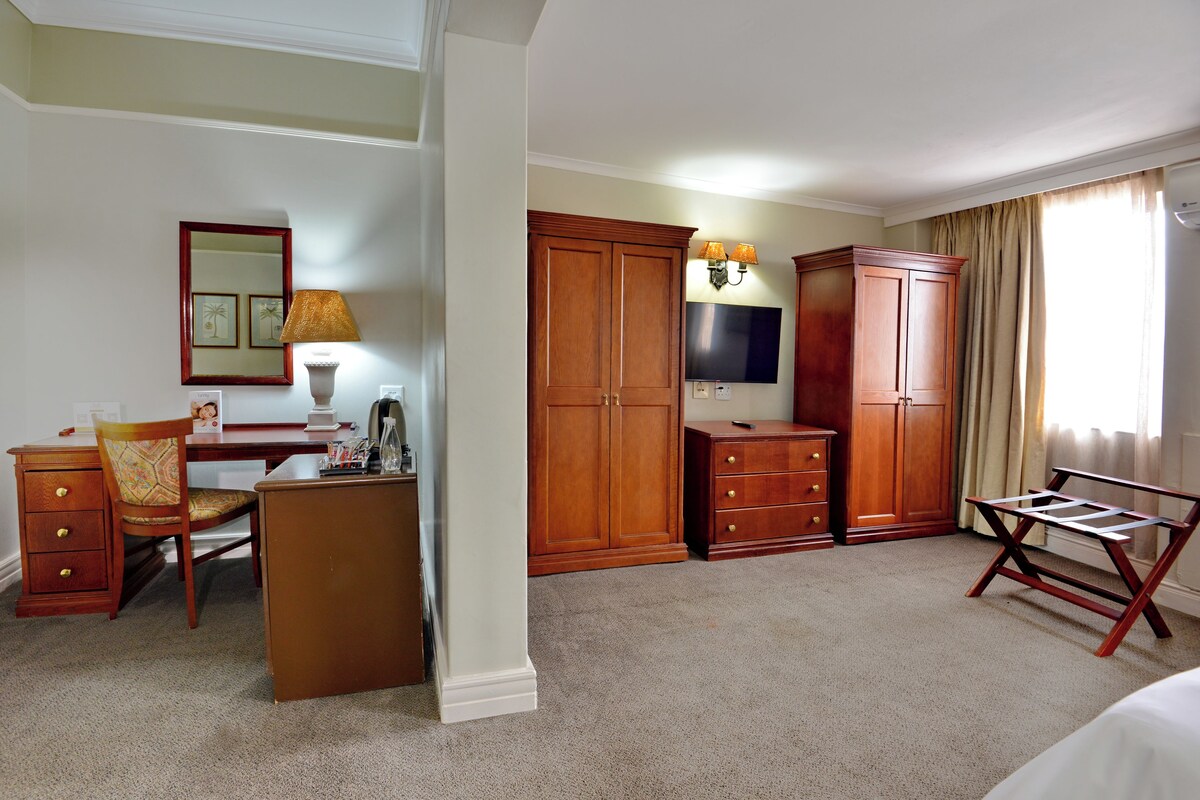 A hotel room with a desk, chair, wardrobe, TV, and a bed.