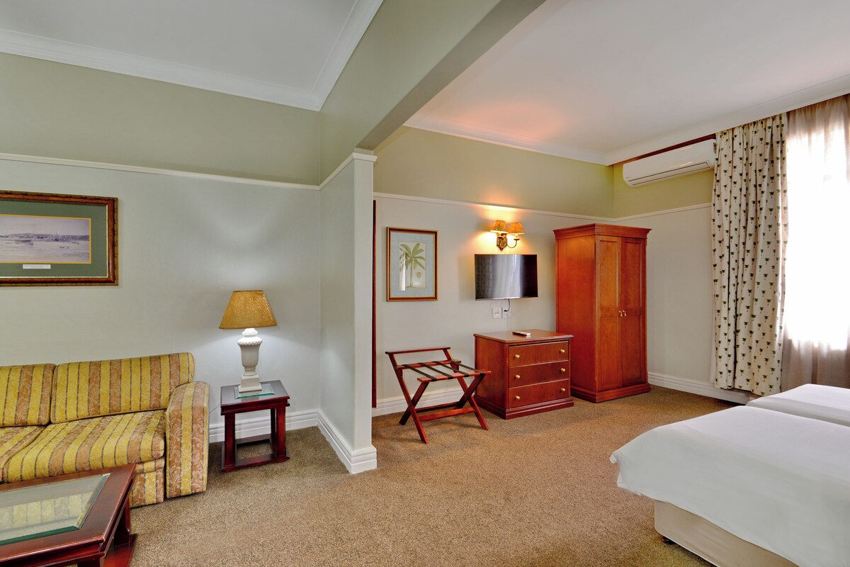 A hotel room with a sofa, a desk, a wardrobe, a bed, and a TV.
