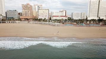Praia com paisagem urbana ao fundo, incluindo edifícios altos e palmeiras.