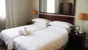 A hotel room with two beds, a large mirror, a nightstand with a lamp, and a patterned curtain. - Balmoral (Durban)