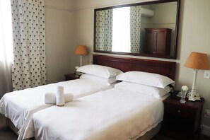 Habitación de hotel con dos camas, un espejo grande, una mesita de noche con lámpara y una cortina estampada.