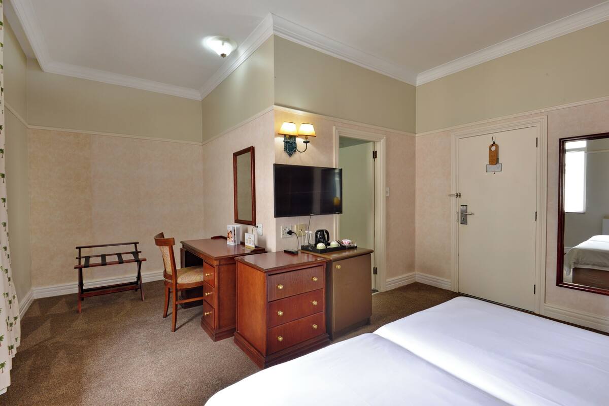 Una habitación de hotel con una cama, un escritorio con silla, un televisor y un armario.