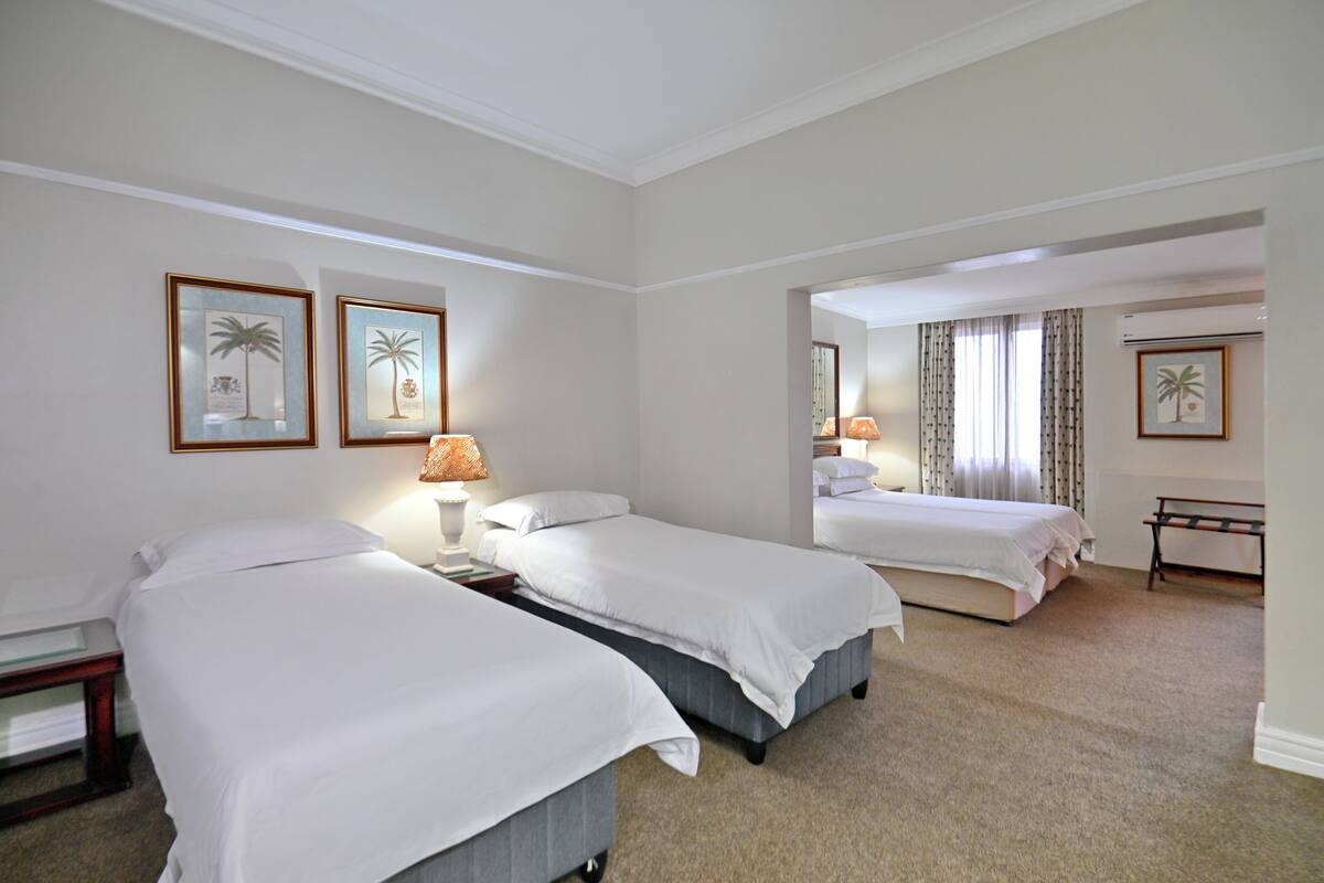 Habitación de hotel con dos camas, una mesita de noche, una lámpara y cuadros en la pared.