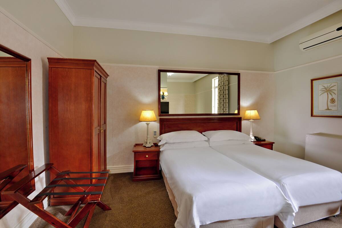Habitación de hotel con una cama doble, dos mesitas de noche, un armario de madera y un espejo en la pared.