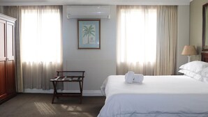 A hotel room with a bed, a wooden bench, a framed picture, and a lamp.