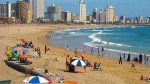 A beach with umbrellas, people, and a city skyline in the background.