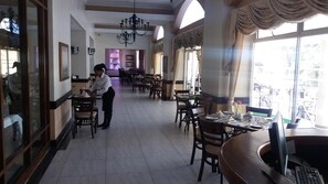 A spacious dining area with multiple tables and chairs, a chandelier, and large windows. - Balmoral (Durban)