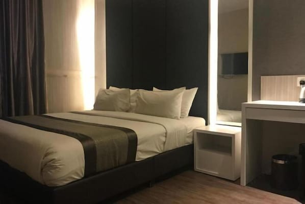 Una habitación de hotel con una cama, mesitas de noche, un espejo y un pequeño armario.