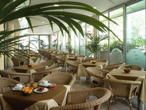 A restaurant with wicker furniture and large windows.