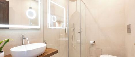 Un baño moderno con ducha envuelta en vidrio, tocador de madera con lavamanos blanco y un inodoro.