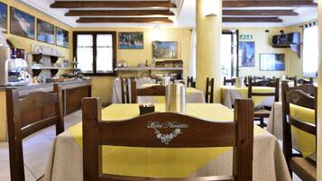 A restaurant with wooden beams on the ceiling, yellow tablecloths, and wooden chairs.