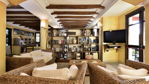 A cozy living room with wicker furniture, a bookshelf, and a television. - Nicoletta Hotel (Baunei)