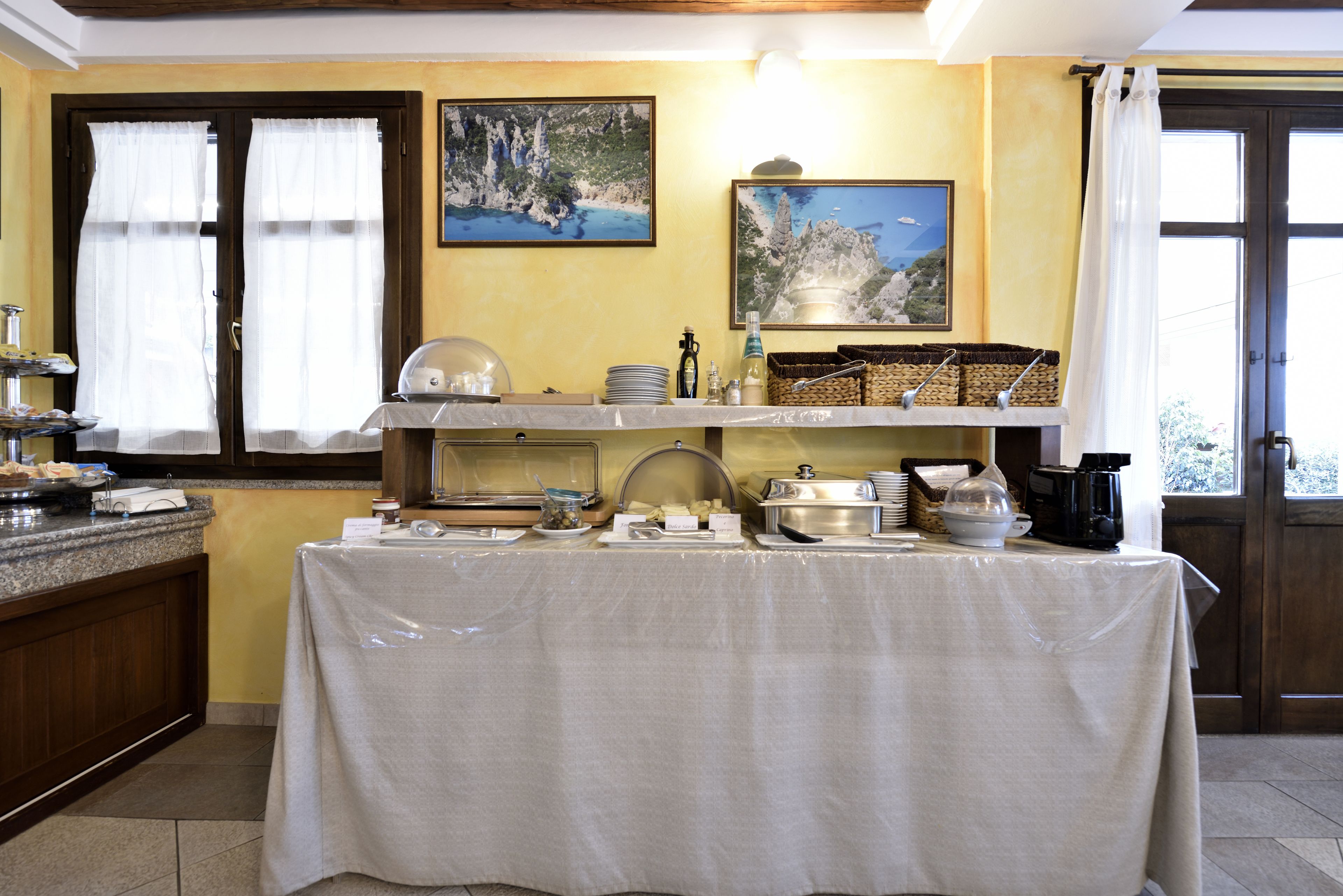 Mesa con una variedad de alimentos y recipientes, junto a ventanas y obras de arte en las paredes.