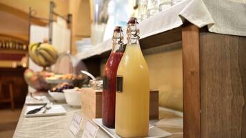A buffet table with two bottles of juice and a bowl of fruit.