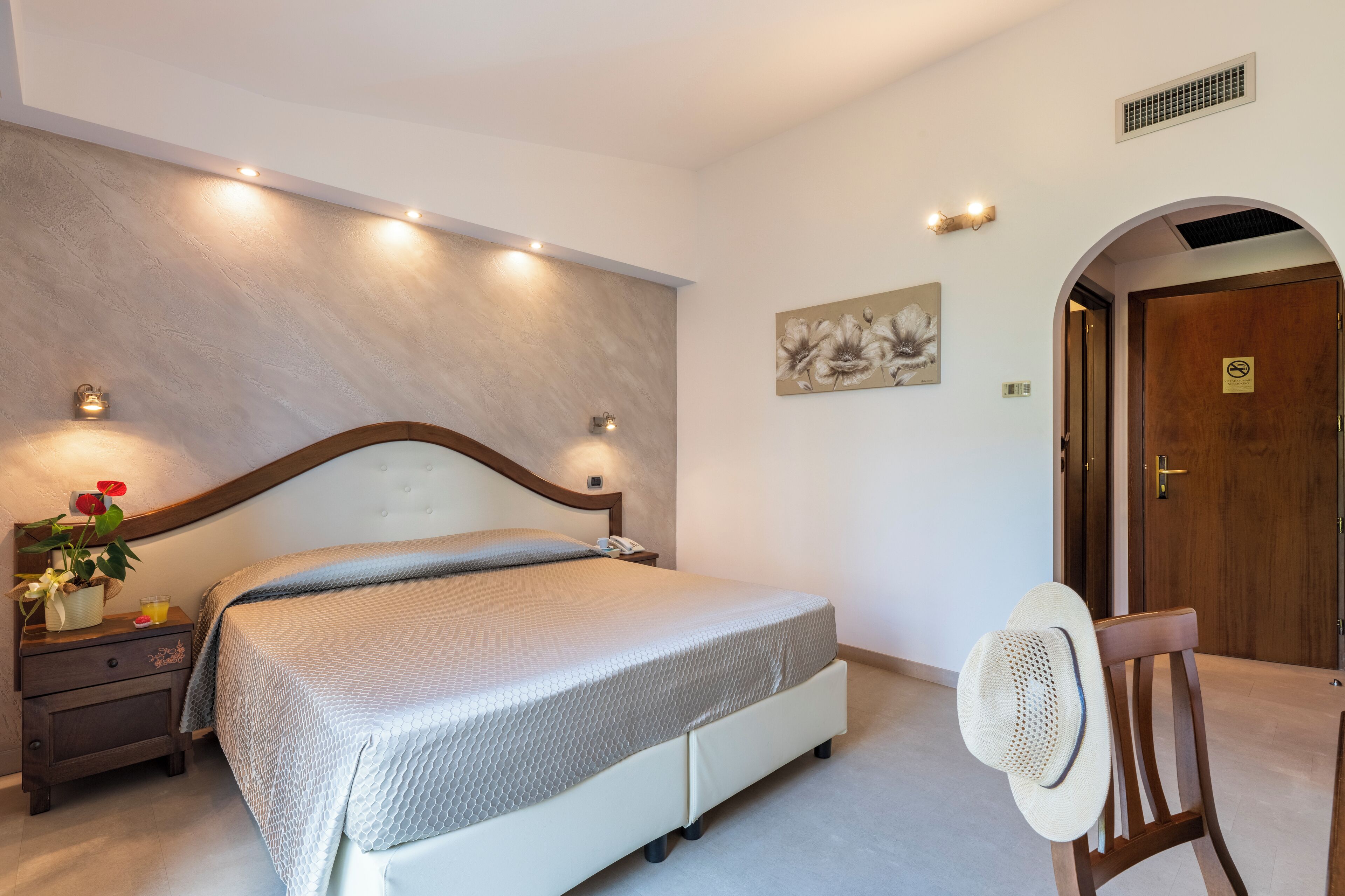 Une chambre à coucher avec un lit, une table de chevet, une lampe et un chapeau posé sur une chaise.