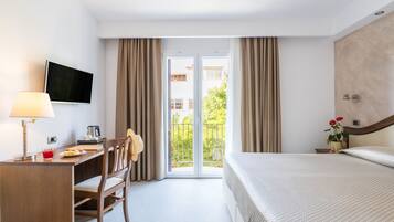 Habitación de hotel con cama, escritorio con lámpara, silla, televisor y balcón con cortinas.