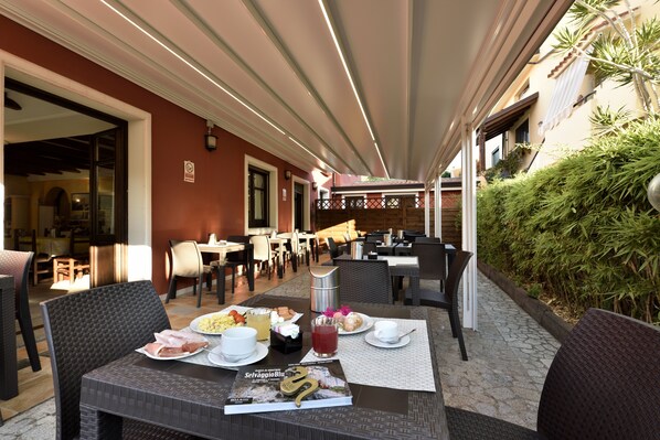 An outdoor dining area with tables and chairs, a menu, and a beverage. - Nicoletta Hotel (Baunei)