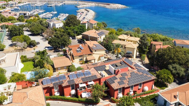 A coastal residential area with houses featuring red-tiled roofs and solar panels. - Nicoletta Hotel (Baunei)