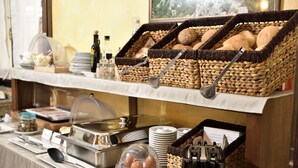 A buffet setup with wicker baskets of bread, a covered hot food station, and various condiments. - Nicoletta Hotel (Baunei)