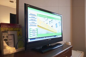 A hotel room with a television displaying a hotel selection interface, a remote control, and a hotel cinema guide book.