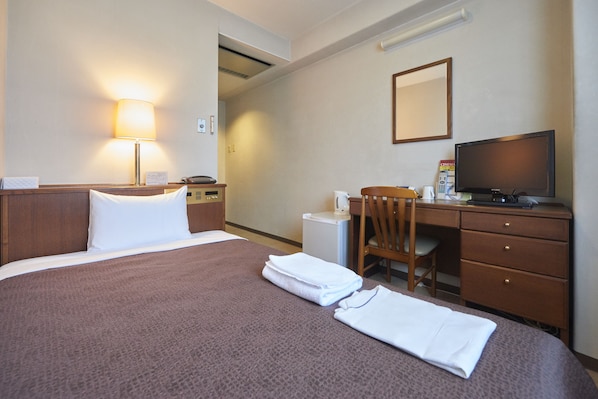 Una habitación de hotel con cama, escritorio, silla, televisor y un refrigerador pequeño.