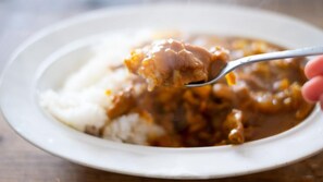 Un plato blanco con una cucharada de comida, posiblemente un guiso o curry, sobre arroz blanco.