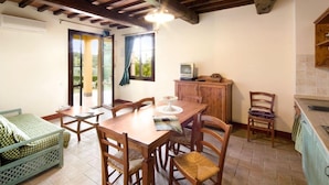 A dining area with a wooden table and chairs, a television on a cabinet, and a view through a glass door.