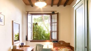 A room with two beds, a wooden table, a chair, a window with curtains, and a cabinet.