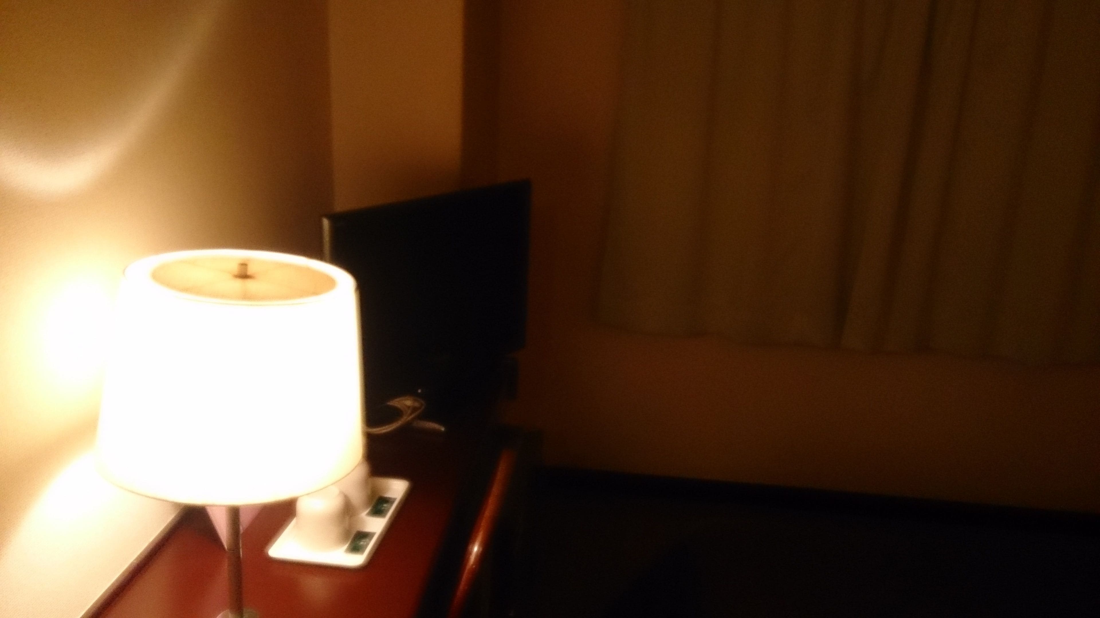 Una habitación con una mesita de noche, una lámpara y un televisor.