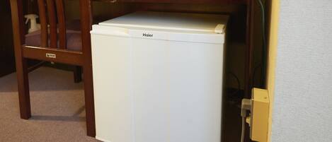 A compact white Haier refrigerator under a wooden desk with a chair, a power outlet, and a cable visible.