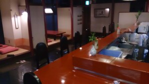 Un restaurant avec un long comptoir, des chaises et une petite table. On y trouve un évier et une plante sur le comptoir.