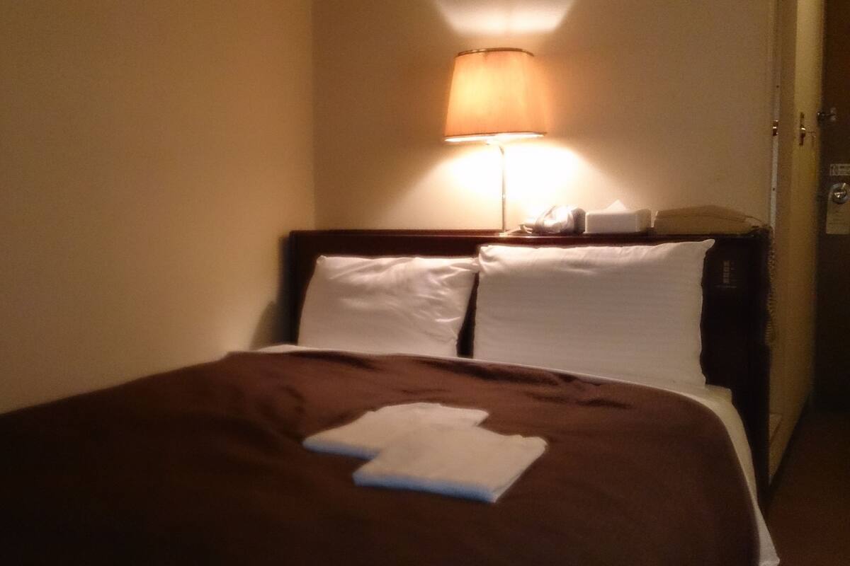 A hotel room with a bed, a nightstand, and a lamp.