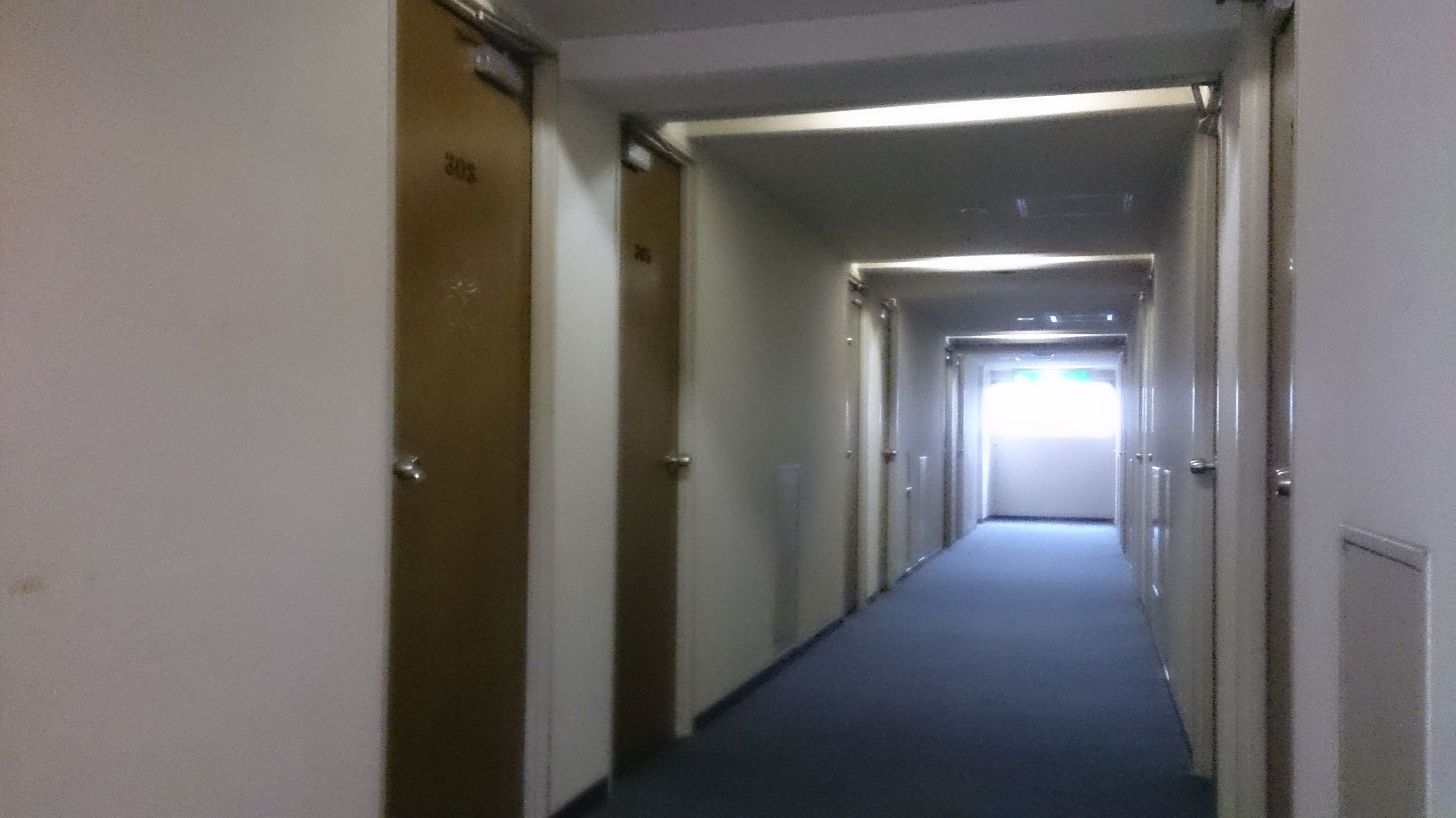 A long, narrow hotel corridor with doors on both sides, leading to individual rooms.