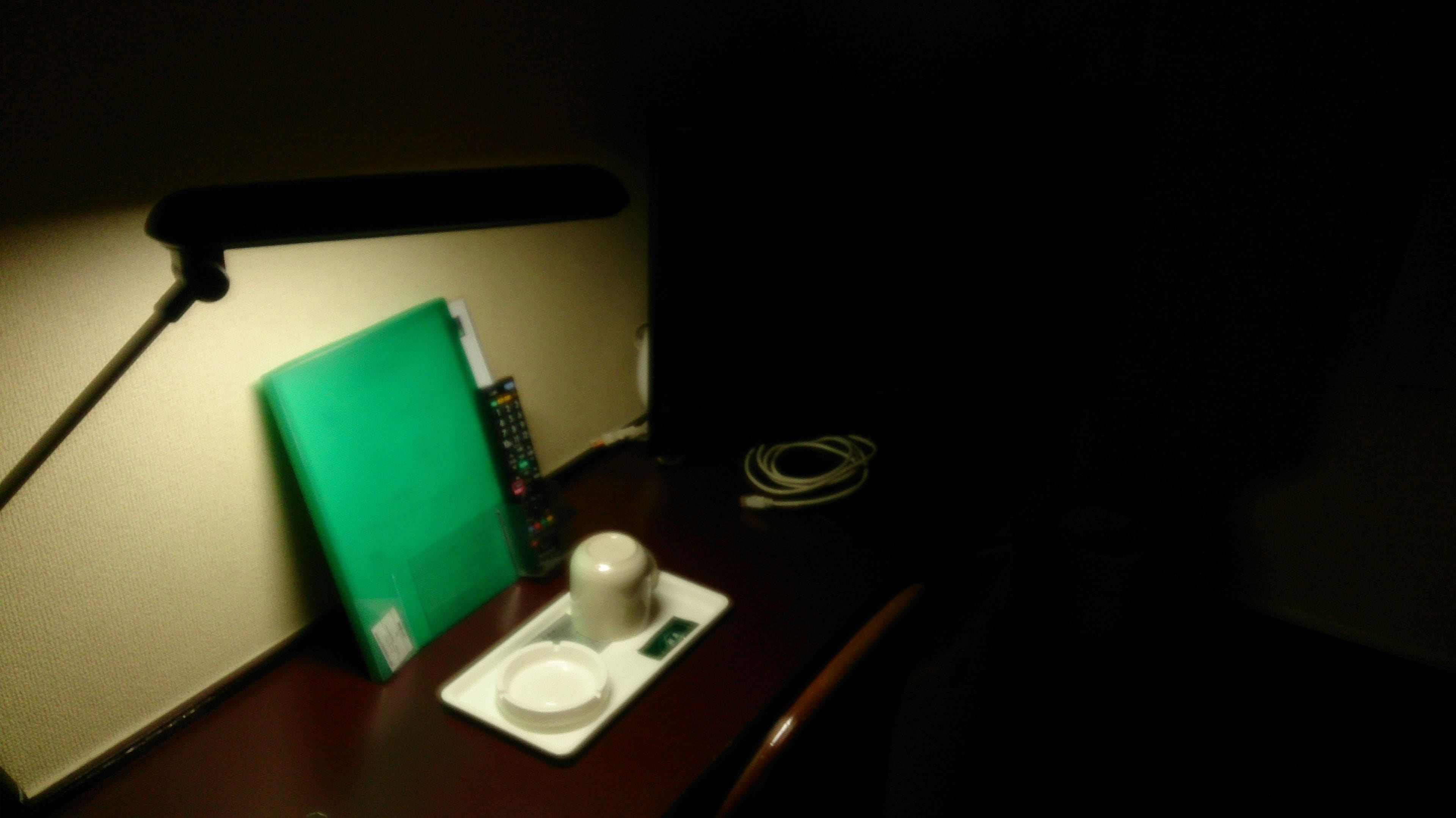 A dimly lit room with a green folder, a white cup, and a remote control on a wooden surface.